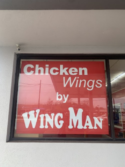 Sign for "Chicken Wings by Wing Man" displayed in a window, featuring bold red and white text.
