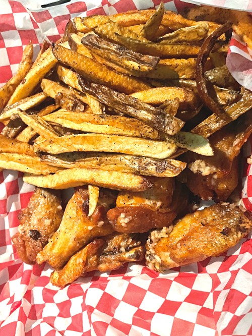 A basket filled with crispy chicken wings and golden French fries, lined with red and white checkered paper.
