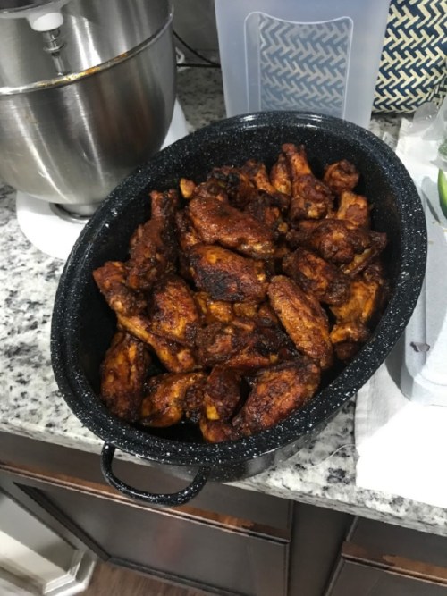 A black roasting pan filled with golden-brown, seasoned chicken wings on a kitchen countertop.