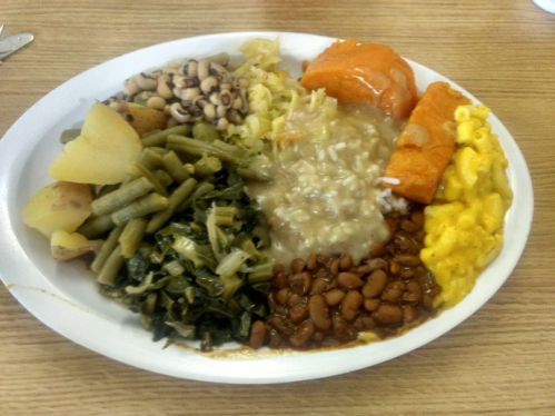 A plate of Southern-style food featuring greens, black-eyed peas, potatoes, macaroni and cheese, and a sweet potato dish.