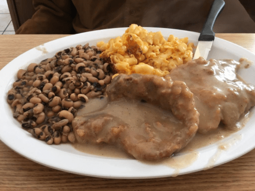A plate of food featuring two pork chops in gravy, black-eyed peas, and macaroni and cheese.