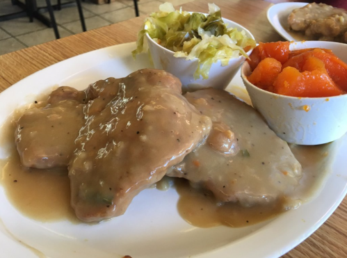 A plate with three pieces of meat covered in gravy, served with a side of lettuce and a bowl of orange squash.