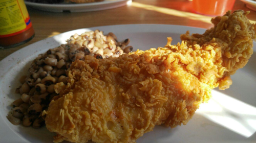 A plate featuring a crispy fried chicken leg next to a serving of black-eyed peas.
