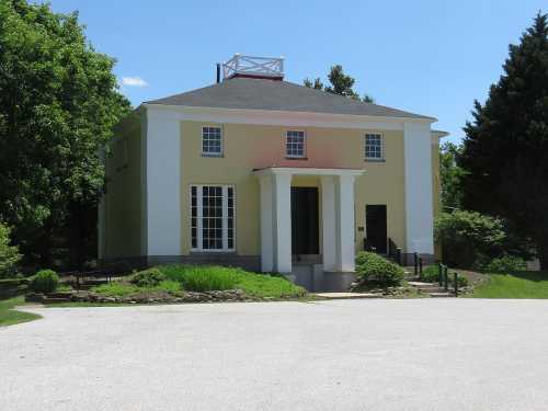 A two-story house with a yellow and white facade, featuring large windows and a front porch, surrounded by greenery.