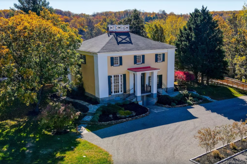 Aerial view of a large, two-story house surrounded by colorful trees and landscaped gardens.