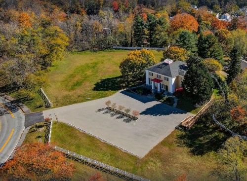 Aerial view of a house surrounded by colorful autumn trees and a spacious parking area.