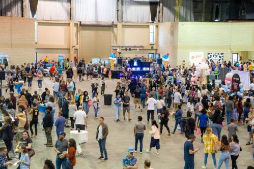 A large crowd gathers in a spacious venue filled with booths and decorations, enjoying an event or festival.
