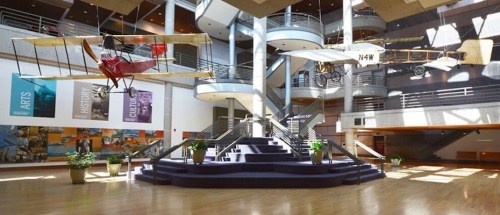 A spacious atrium with hanging vintage aircraft, surrounded by plants and modern architecture.