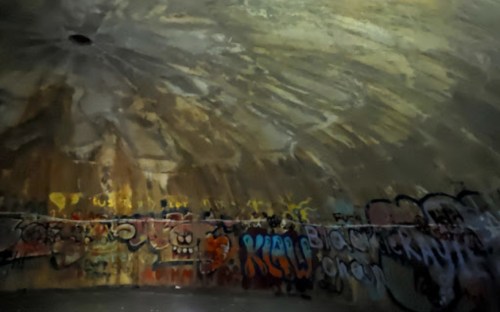 Interior of a dome-shaped structure with colorful graffiti on the walls and a textured, faded ceiling.