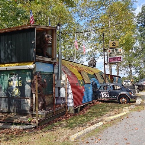 Colorful roadside attraction featuring a quirky building, a vintage taxi, and playful sculptures.