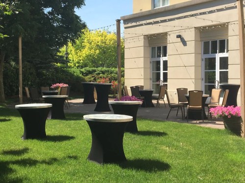 Outdoor seating area with round tables, chairs, and colorful flowers under a clear blue sky.