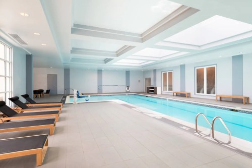 Indoor swimming pool area with lounge chairs, large windows, and a bright, airy atmosphere.