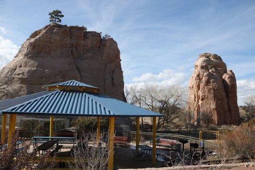 A gazebo with a blue roof surrounded by rock formations and trees under a partly cloudy sky.
