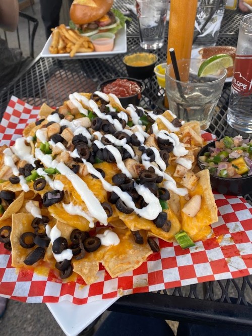 A large plate of nachos topped with chicken, black olives, sour cream, and green onions, served with salsa on the side.