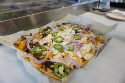 A plate of nachos topped with cheese, jalapeños, onions, and beef, served on parchment paper.