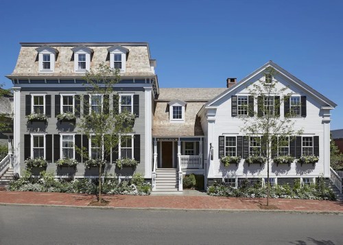 A charming two-story house with white siding, green shutters, and flower boxes, set against a clear blue sky.