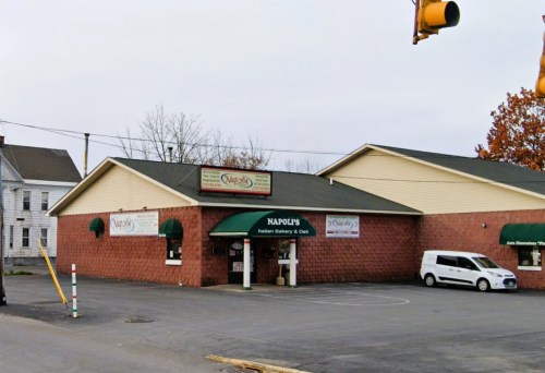 Exterior of Napole's Italian Bakery & Deli, featuring a brick facade and green awnings, with a parking lot in front.