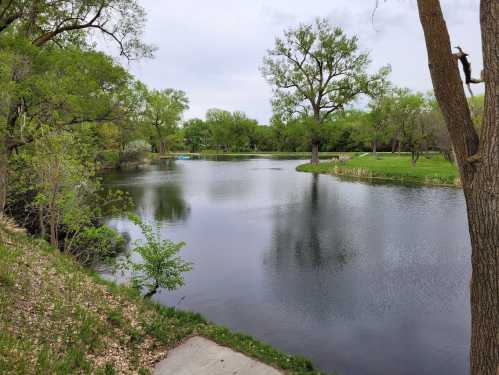 A serene pond surrounded by lush greenery and trees under a cloudy sky.