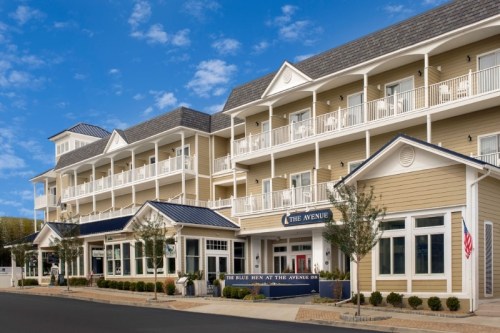 A charming hotel with a light-colored facade, balconies, and a welcoming entrance under a blue sky.