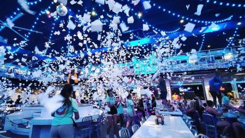 A lively party scene with people celebrating under blue lights, surrounded by falling confetti and a festive atmosphere.