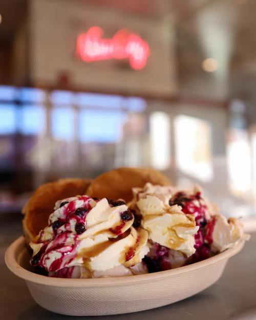 A close-up of a bowl of ice cream topped with berry sauce, set against a blurred background of a shop.