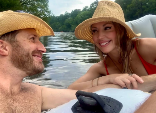 A couple smiles at each other while relaxing on a river in inflatable rafts, wearing straw hats.
