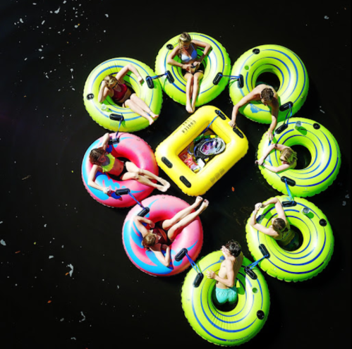 Aerial view of colorful inner tubes on water, with people relaxing in them on a sunny day.