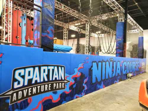 A colorful indoor ninja course at Spartan Adventure Park, featuring climbing walls and hanging obstacles.