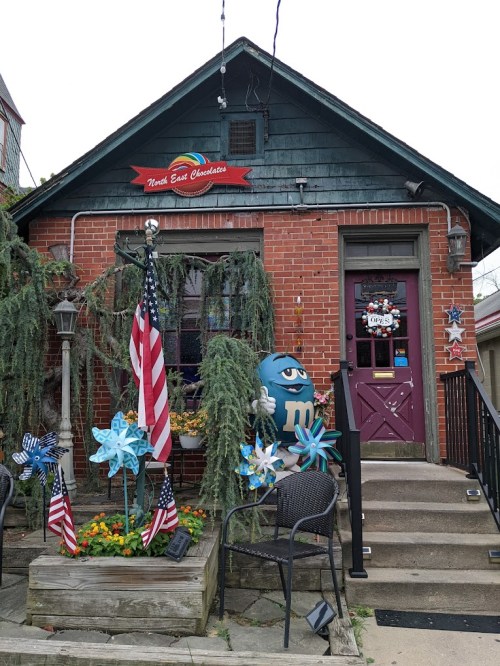 A charming brick building with a colorful sign, American flags, and decorative pinwheels in front.