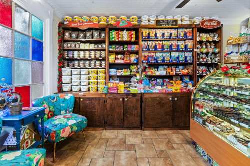 A colorful shop interior with shelves filled with various snacks and candies, and a display case of desserts.