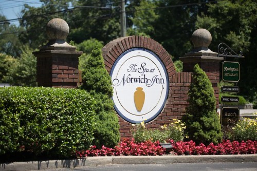 Sign for The Spa at Norwich Inn, featuring brick pillars, greenery, and colorful flowers in front.