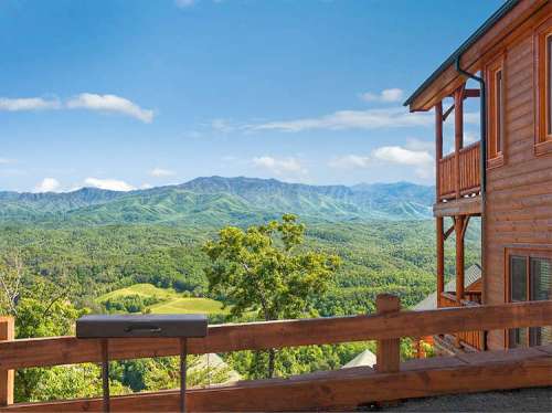 Scenic mountain view from a wooden balcony, featuring lush green hills and a clear blue sky.