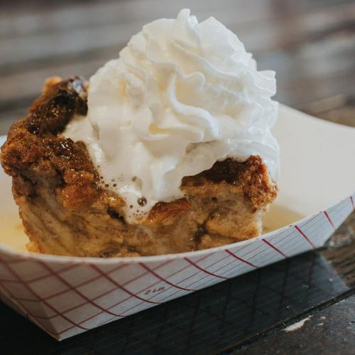 A delicious dessert featuring a warm, gooey bread pudding topped with a generous swirl of whipped cream.