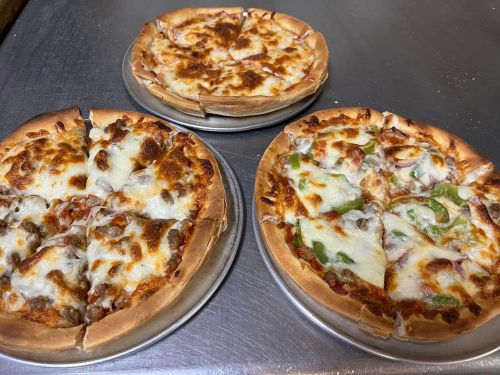 Three pizzas on metal trays: one with pepperoni, one with sausage, and one with green peppers and onions.