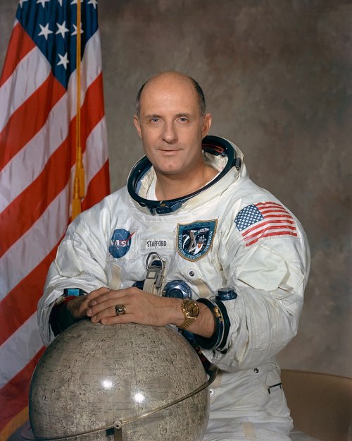 Astronaut in a space suit poses with a globe, an American flag in the background.