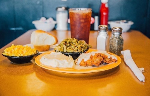 A plate of fried chicken, mashed potatoes, green beans, and corn, with a roll and iced tea on a diner table.