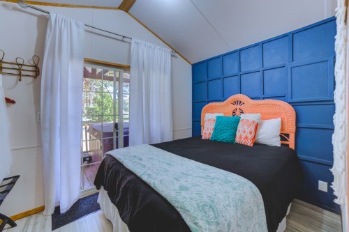 Cozy bedroom with a black bedspread, colorful pillows, and a door leading to an outdoor area. Bright and inviting decor.
