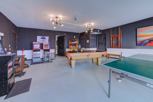 A game room featuring a pool table, ping pong table, arcade machines, and a cozy seating area.