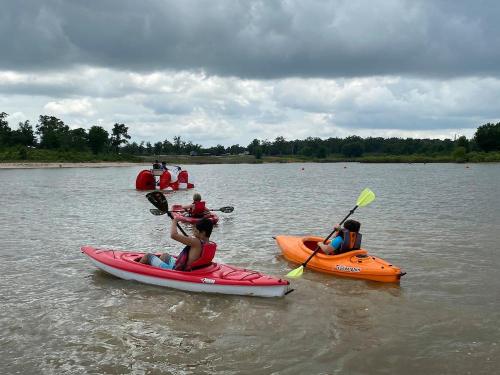 Two people kayak on a calm water body under a cloudy sky, with a red structure in the background.