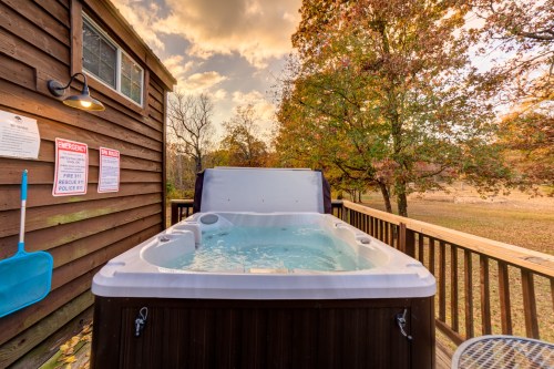A hot tub on a wooden deck surrounded by autumn trees and a cloudy sky. Signs for emergency and fire safety are visible.