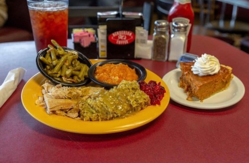 A plate with turkey, stuffing, green beans, cranberry sauce, and a slice of pumpkin pie with whipped cream on the side.