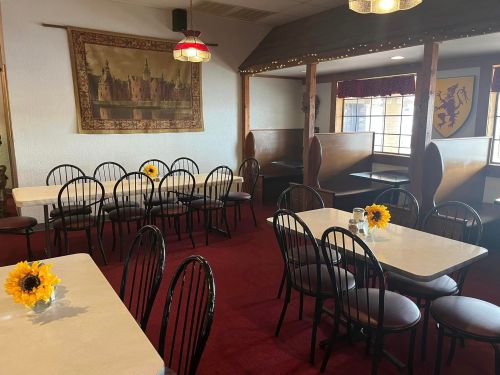Cozy restaurant interior with tables, black chairs, and sunflower centerpieces, featuring a tapestry on the wall.