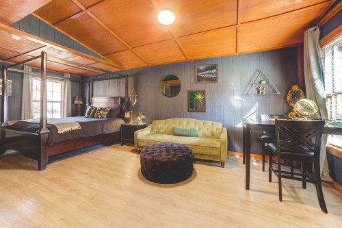 Cozy bedroom with a four-poster bed, green sofa, round ottoman, and a small dining table in a warmly lit space.