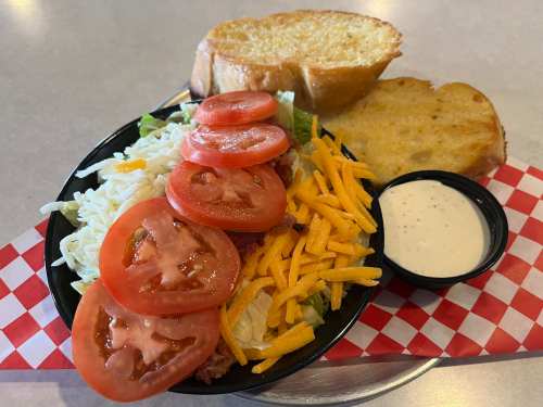 A colorful salad with lettuce, tomatoes, cheese, and ranch dressing, served with two slices of toasted garlic bread.