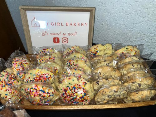 A wooden tray filled with assorted cookies, some topped with colorful sprinkles, next to a sign for "My Girl Bakery."