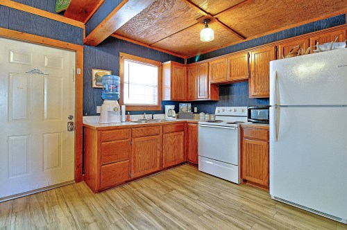 Bright kitchen with wooden cabinets, white appliances, and a water cooler, featuring a door and window for natural light.