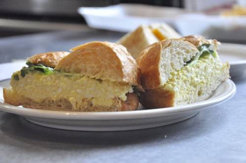 A plate with two croissant sandwiches filled with egg and lettuce, showcasing a flaky, golden-brown exterior.
