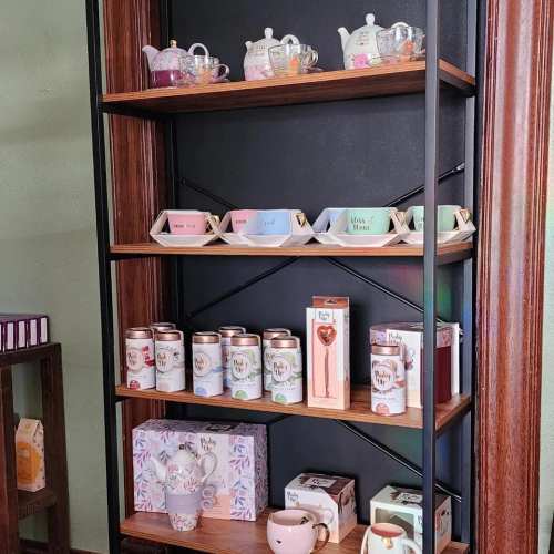 A wooden shelf displaying colorful teapots, cups, and tea canisters, with decorative items arranged neatly.