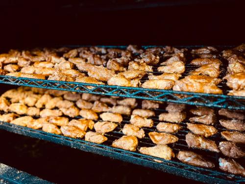 Close-up of two racks of smoked meat, showcasing a variety of golden-brown pieces in a dark smoker.