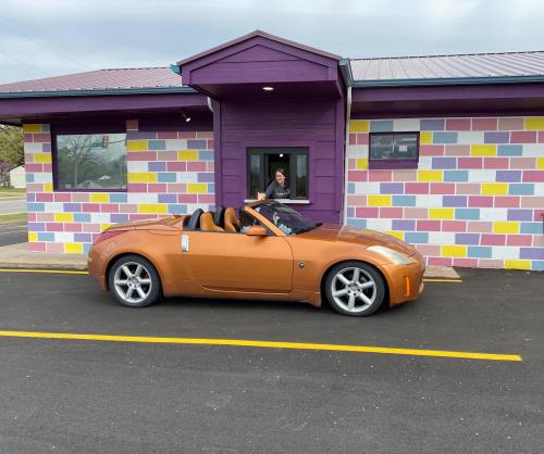 A convertible orange car parked in front of a colorful building with a person visible inside.